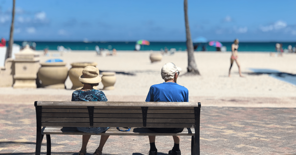 A male and female sitting on bench at beach discussing retirement