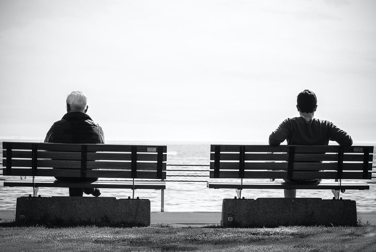 black and white photo of the back of two men sitting on separate park benches